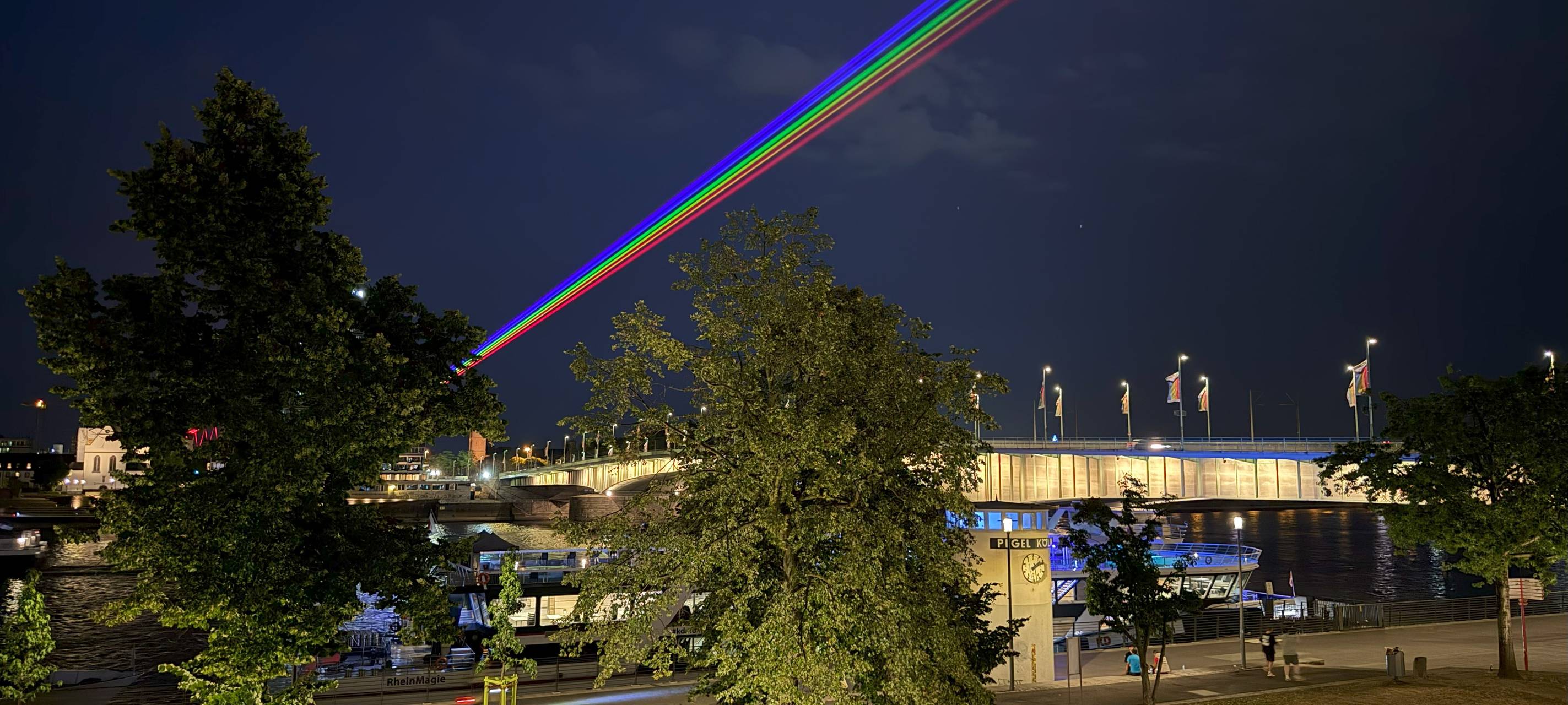 Ein Laser über Deutz und den Rhein in Regenbogenfarben.