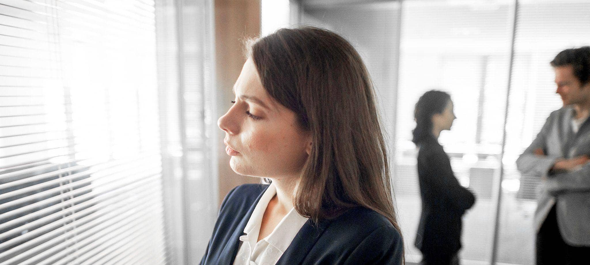 Frau steht abseits ihrer Kollegen in einem Büro